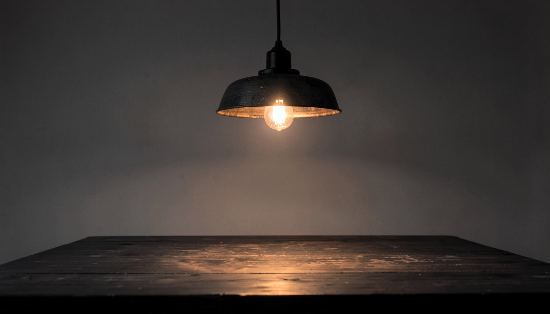 Detail van een hangende lamp boven een tafel, met warm gloeilicht en donkere houten textuur.